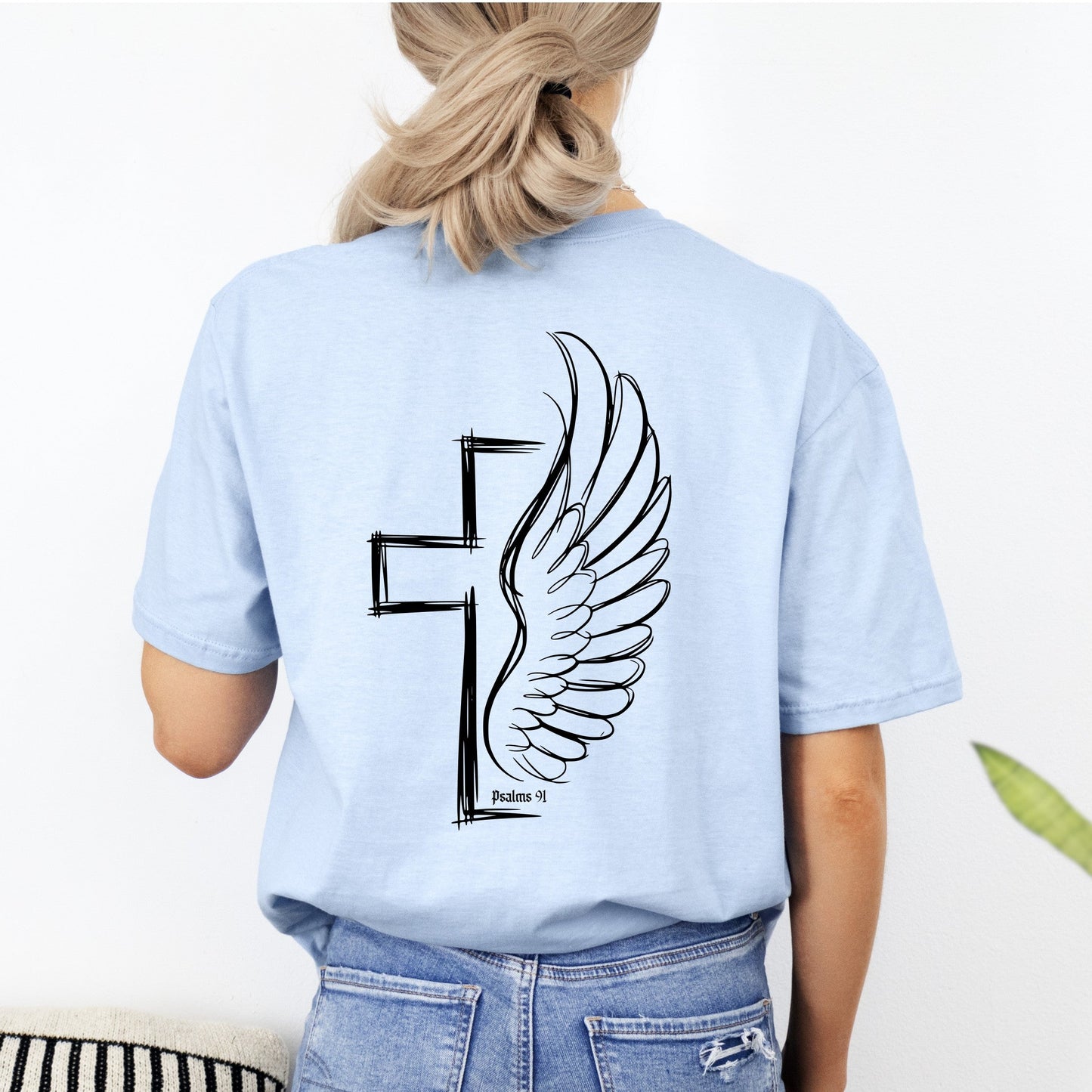 Light blue t-shirt with a cross and wing design on the back, worn by a person.