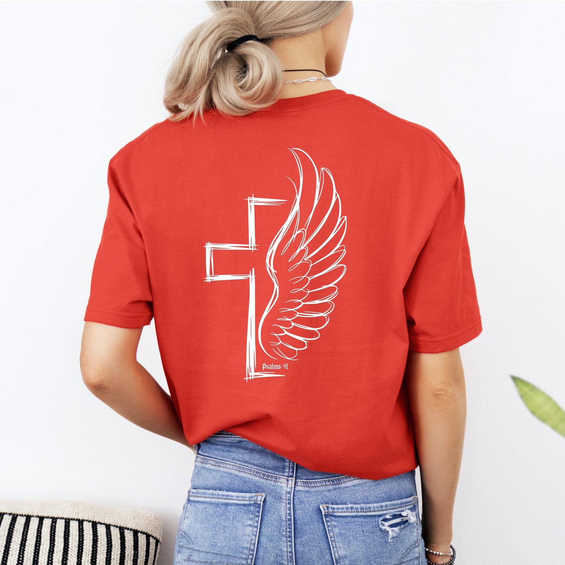 Person wearing a red t-shirt with a white winged cross design on the back, standing against a light background.
