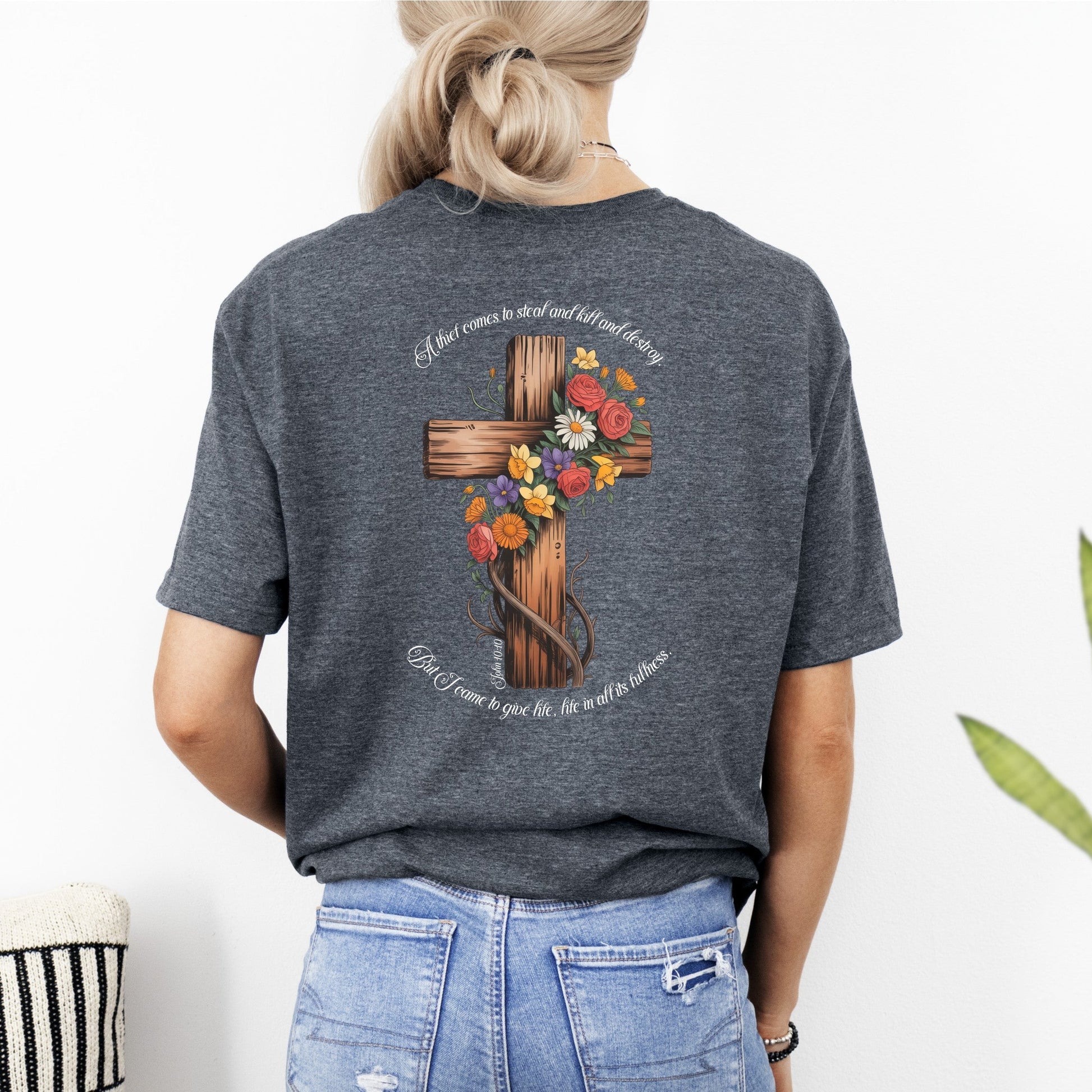 Person wearing a gray t-shirt with a cross and floral design on the back, standing against a white background.