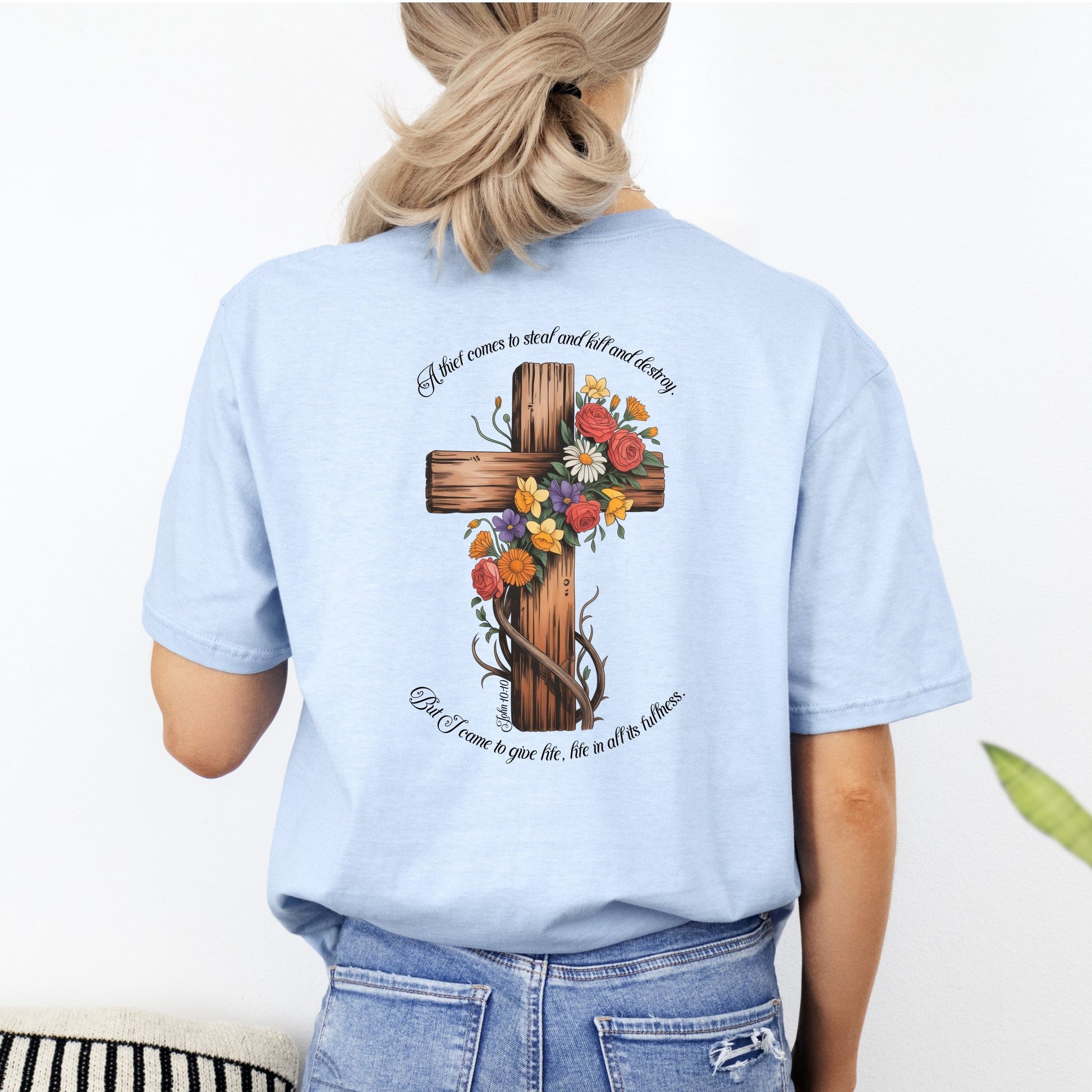 Light blue t-shirt with a cross and floral design on the back, worn by a person.