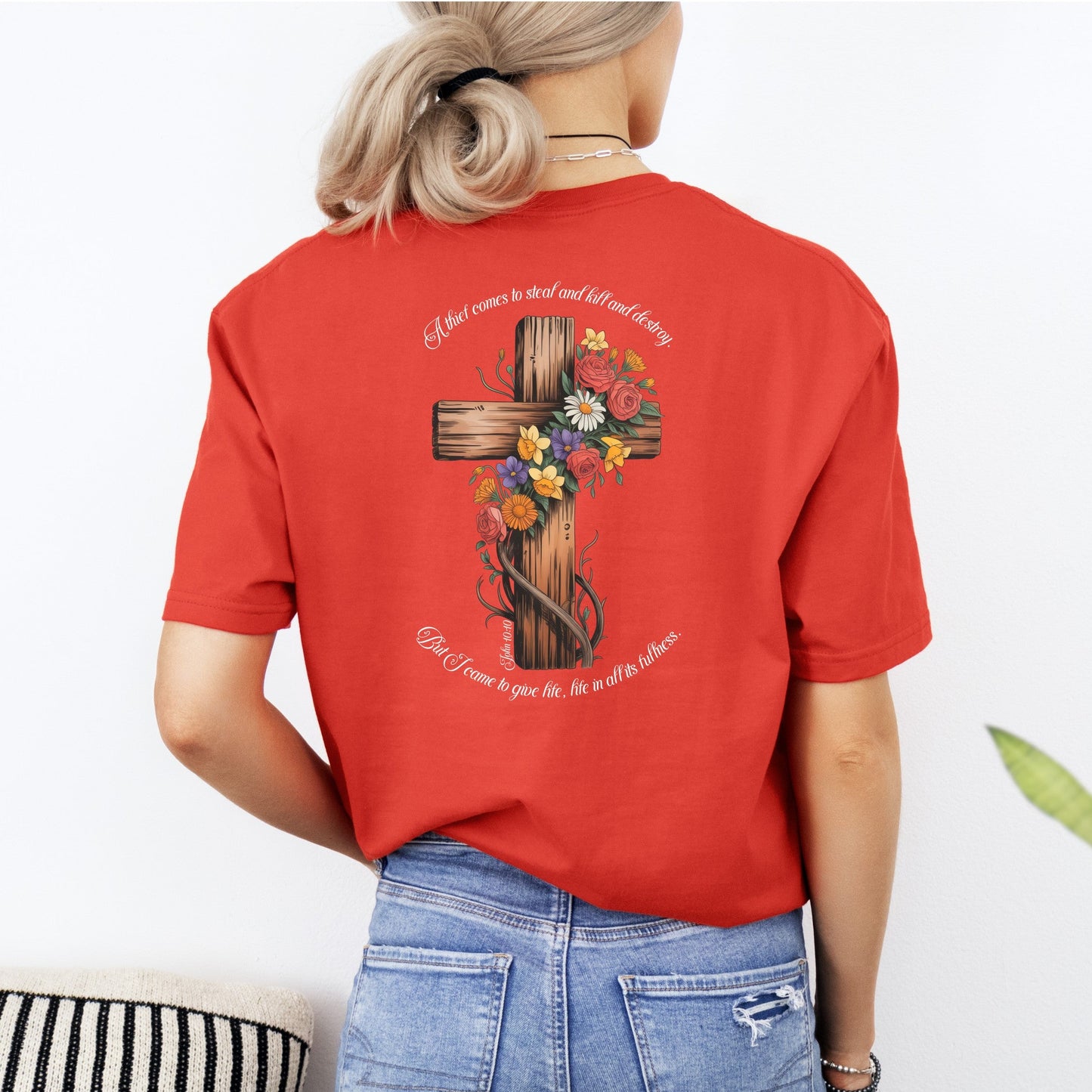 Person wearing a red t-shirt with a floral cross design on the back, standing against a white background.