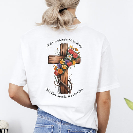 Person wearing a white t-shirt with a cross design and text, standing against a plain background.