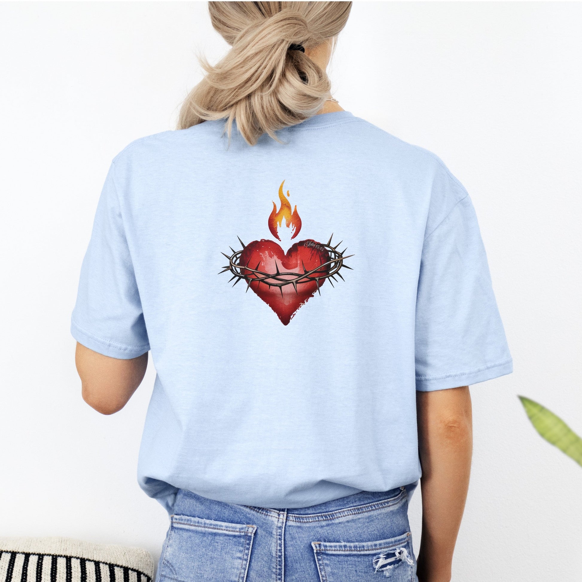 Person wearing a light blue t-shirt with a heart design on the back, standing against a white background.
