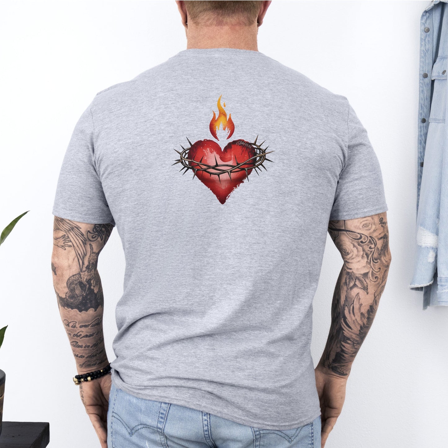 Person wearing a gray t-shirt with a heart design on the back, standing against a white wall.